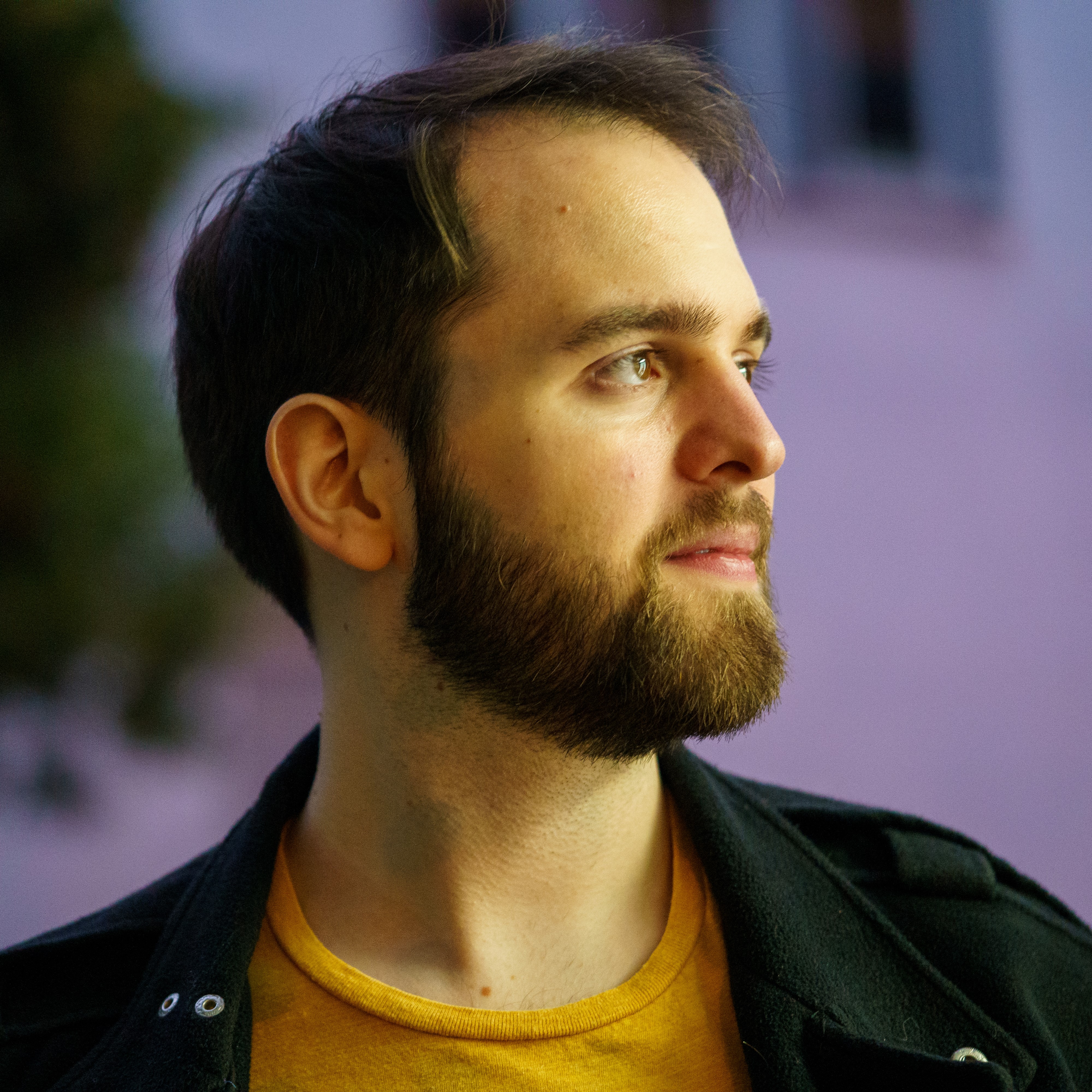 Photograph of me (Kevin), wearing a yellow shirt and a black jacket, in front of a blurry background.